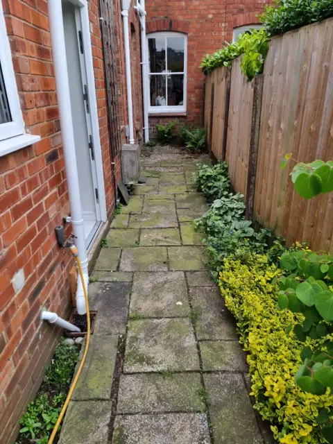 Narrow side passage with mossy, weed-filled concrete slabs before the makeover